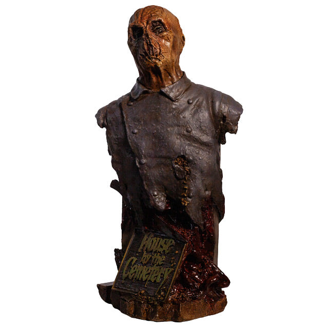Zombie bust, front view, head, shoulders and chest. Orange-hued shriveled flesh, wearing filthy and gory blue doctor's coat. Gore coming from bottom of torso. Plaque at bottom, gold text reads House by the Cemetary, on wood look base.