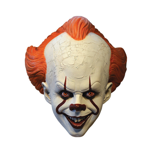 Mask, front view. IT clown face, red hair, white cracked skin, large forehead, red eyes and nose, dark lips, creepy smile with crooked buck teeth.