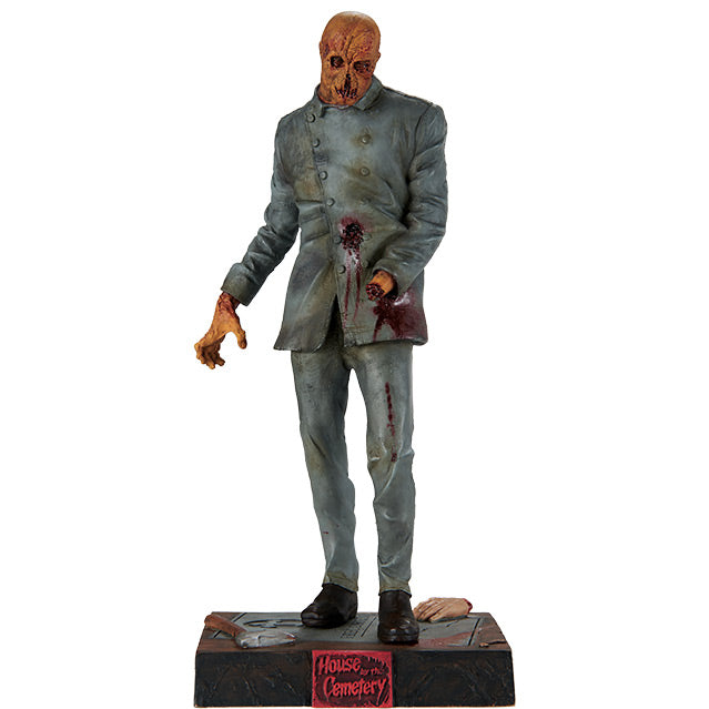Statue, front view.  Zombie figure, orange hued decaying flesh, wearing distressed, dirty, bloodied blue doctor's coat and blue pants, black shoes, missing left hand.  Standing on black, dirty base, severed hand and hatchet are resting on base, plaque on front red text reads house by the Cemetary.