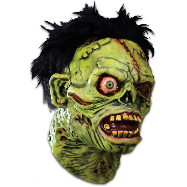 Mask, right side view.  Black bushy hair, Green flesh, wrinkled and wounded.  Bulging, bloodshot right eye, missing left eye and nose.  Open snarling mouth with yellow crooked teeth. 