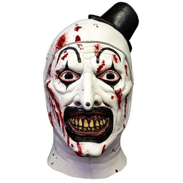 Mask, head and neck, front view. Evil grinning, black and white clown face with blood spatter, high black painted eyebrows, black around eyes and mouth, black dot on tip of nose, pink gums and yellow teeth. wearing tiny black top hat.