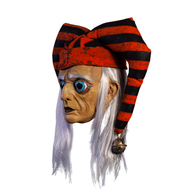 Mask, left view. Long, straight white hair, white eyebrows. Large ears. Large round blue eyes with very large pupils. Mouth closed, dark lips. Wearing dirty orange and black striped jester hat with bells on ends.