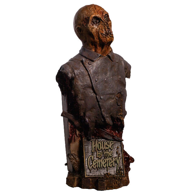 Zombie bust, right view, head, shoulders and chest. Orange-hued shriveled flesh, wearing filthy and gory blue doctor's coat. Gore coming from bottom of torso. Plaque at bottom, gold text reads House by the Cemetary, on wood look base.