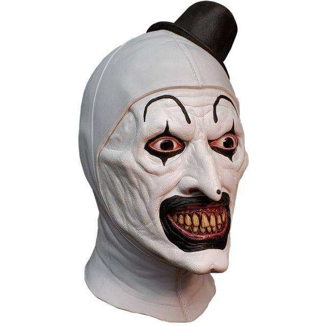 Mask, head and neck, right side view. Evil grinning, black and white clown face, high black painted eyebrows, black around eyes and mouth, black dot on tip of nose, pink gums and yellow teeth. wearing tiny black top hat.