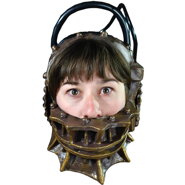 Mask, front view, on person's head. Metallic gold trap-like device that fits around lower head and neck and over top from side to side, gears on side. black handle and cords.