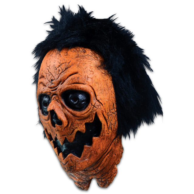 Mask, head and neck, left side view. Black hair, orange distressed flesh. Black eyes, nose and mouth made to resemble a jack o' lantern.