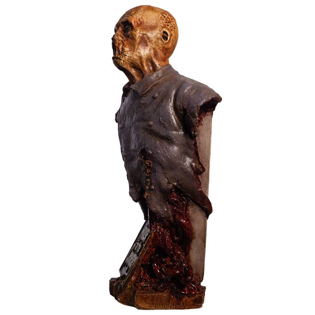 Zombie bust, left side view, head, shoulders and chest. Orange-hued shriveled flesh, wearing filthy and gory blue doctor's coat. Gore coming from bottom of torso. Gray tombstone in back, set on wood look base.