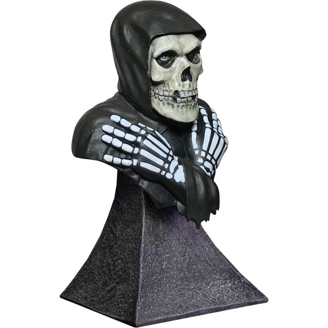 Mini bust, right side view. Head, shoulders and upper chest. Misfits Fiend, skeleton face and hands, crossed, wearing black hooded cloak. Set on gray stone textured base.