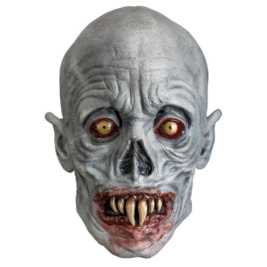 Mask, front view. Bald, gray wrinkled skin, no eyebrows, sunken yellow and red eyes, pointed ears, skeletal nose,  blood-rimmed grimacing mouth, two long central fangs with two smaller fangs on either side.