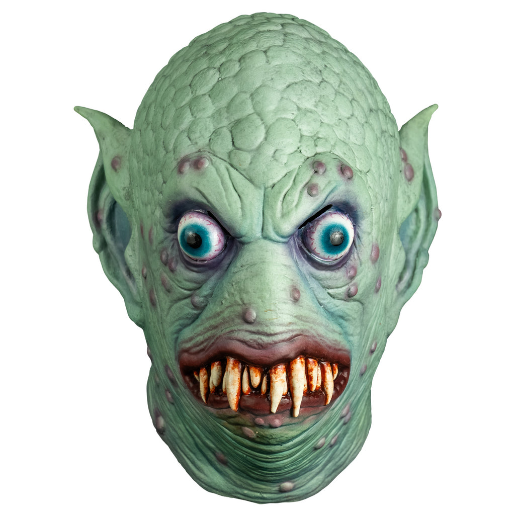 Mask, front view.  Pale blue-green scaly flesh on top of head, wrinkled around eyes, mouth and neck, scattered pale purple bumps on face and ears.  Large pointed ears. Bulging, bloodshot, round aqua blue eyes.  No nose. pale red, lumpy lips slightly open showing may sharp dirty brown teeth.