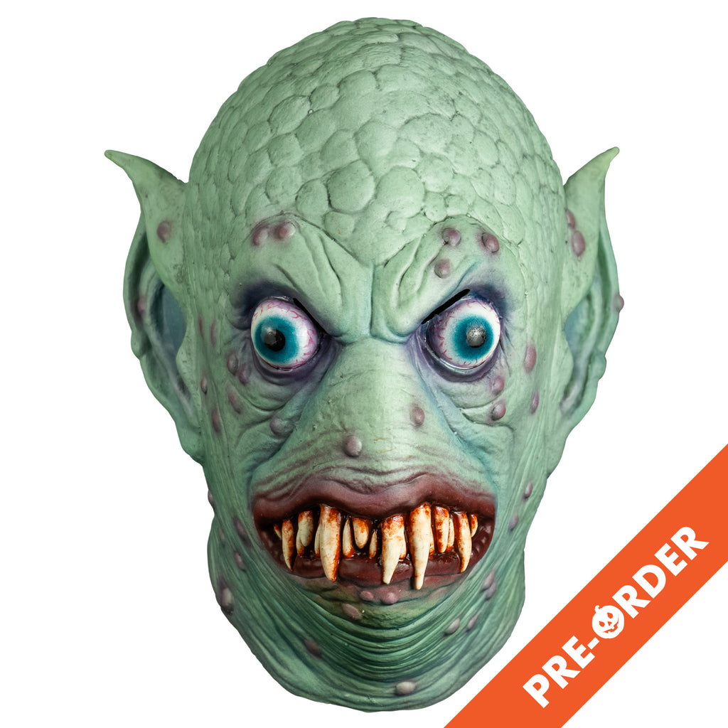 white background, orange diagonal banner bottom right, white text reads pre-order.  Mask, front view. Pale blue-green scaly flesh on top of head, wrinkled around eyes, mouth and neck, scattered pale purple bumps on face and ears. Large pointed ears. Bulging, bloodshot, round aqua blue eyes. No nose. pale red, lumpy lips slightly open showing may sharp dirty brown teeth.