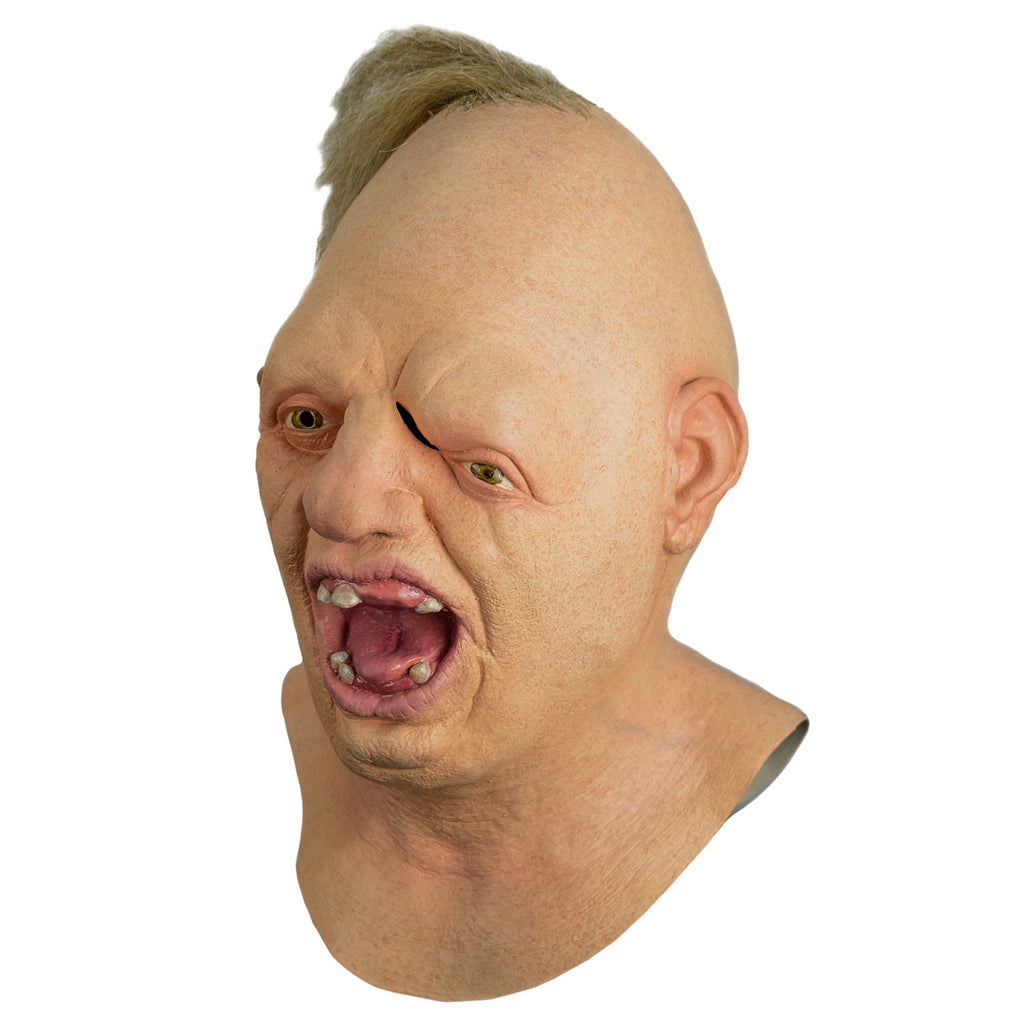 Mask, left side view, head, neck and upper chest. Egg shaped head, tuft of disheveled blond hair on top. No eyebrows, light brown eyes offset, left eye lower than the right. Large crooked nose. Mouth wide open showing pink tongue and gums and only 6 teeth.