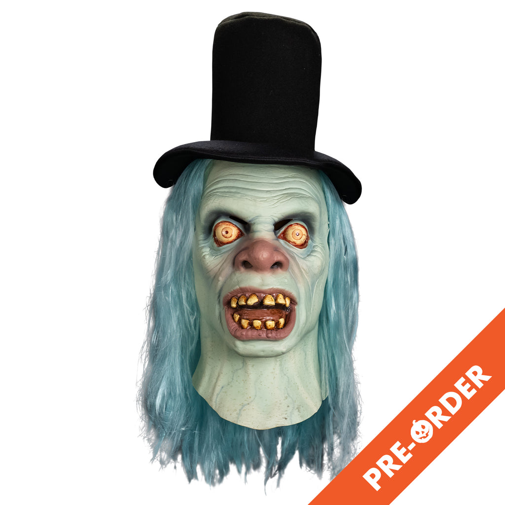 white background, orange diagonal banner bottom right, white text reads pre-order. Mask front view, head and neck. Black top hat. Long, straight, light blue hair. Pale blue wrinkled skin. No eyebrows, large, wide open, bloodshot yellow eyes. Large, bulbous pink nose. Mouth, wide open showing tongue and dirty yellowed teeth, large pink lips. blue veins showing on neck.
