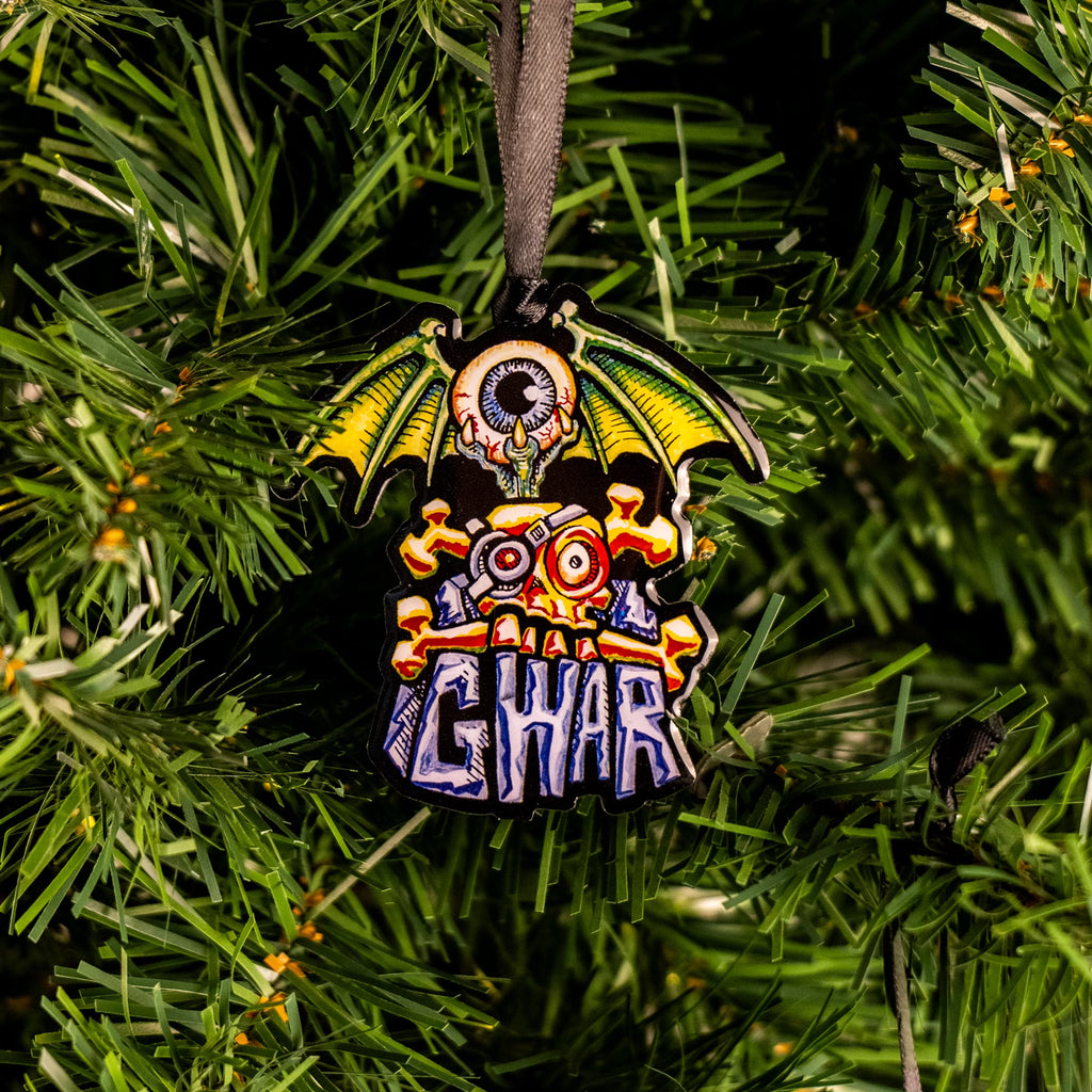 GWAR flying eye matal ornament. hung on Christmas tree.  Blue iris, bloodshot round eyeball, green dragon wings on the sides, held in three-toed claw rising out of orange skull and crossbones set on top of gray stone-like lettering that reads GWAR