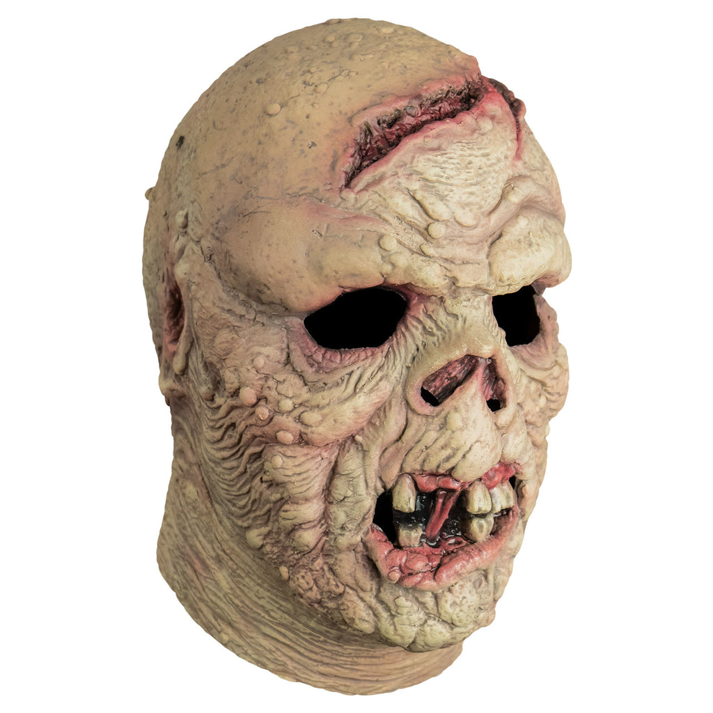 Mask, right side view, head and neck. Bald. Pinkish, wrinkled and lumpy flesh, large open wound on forehead and crown of head. missing nose. Mouth open showing gums, gapped dirty teeth, deformed pink bottom lip.