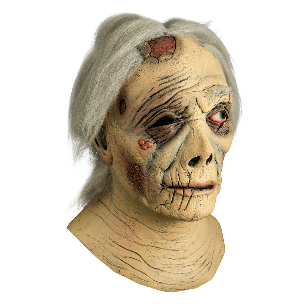 Mask, right side view. Head and neck. Short gray hair, wrinkled and ragged skin. large wound on right side of the forehead. Right eye black, no eyebrow, left eye blue, bloodshot, scar across eye. Sores on right cheekbone. Misshapen nose, mouth slightly open, thin lips.