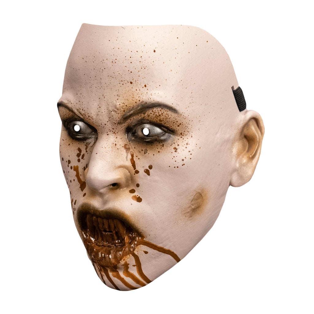 Plastic mask. left side view. pale skin, blood spattered face. brown arched eyebrows, black-rimmed white eyes. mouth with lips open showing sharp bloodstained teeth, blood dripping down chin.