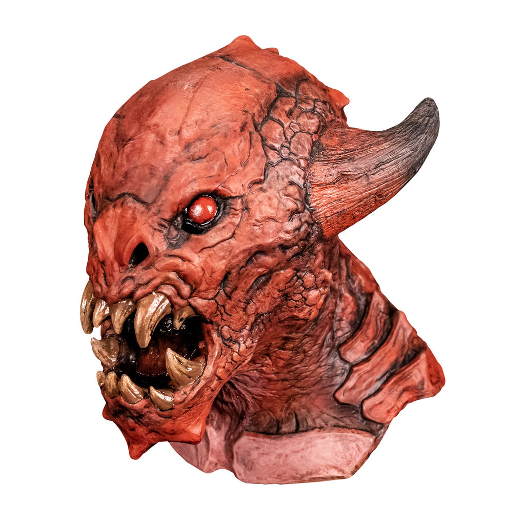 Mask, left side view. Red creature with horns on either side of head, red black-rimmed eyes, snout-like nose, open mouth showing several large yellowed sharp fangs, wrinkled and scaly skin on face pointed chin. Large plate-like scales on neck and chest