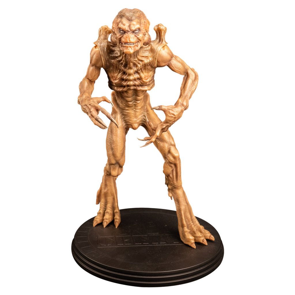 Front view Pumpkinhead 8" scale figure.   Pale orange tan creature with enlarged upper head. White eyes, animal-like muzzle, mouth showing sharp yellow teeth. Bony with defined muscles, protrusions on shoulders, long limbs and tail. Hands have 4 long fingers and claws. Animal-like 3 toed feet with bony protrusions on heels, short claws. standing on black round platform.