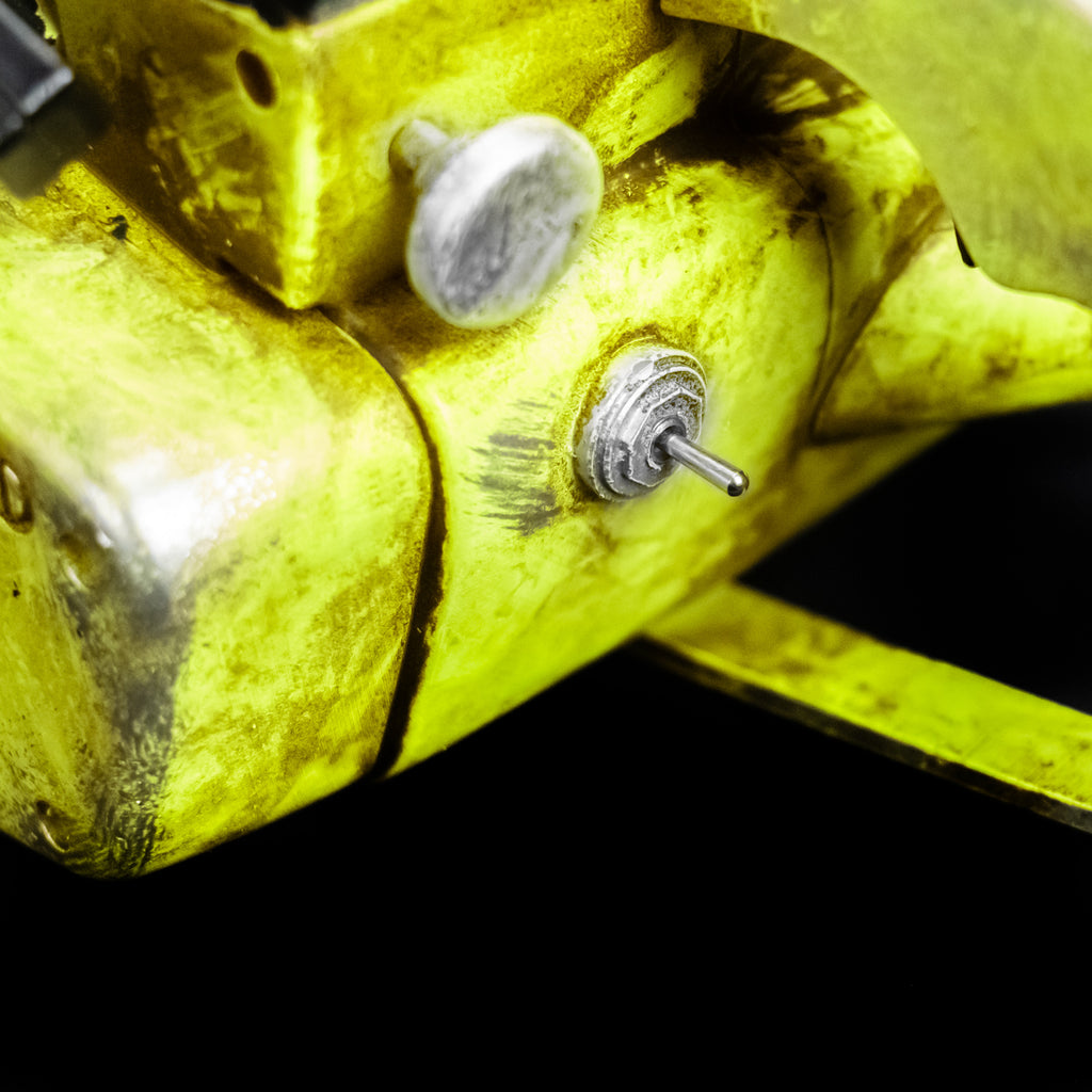 Black background. Chainsaw prop. Close-up view of silver toggle switch and knob. Distressed weathered yellow body. 