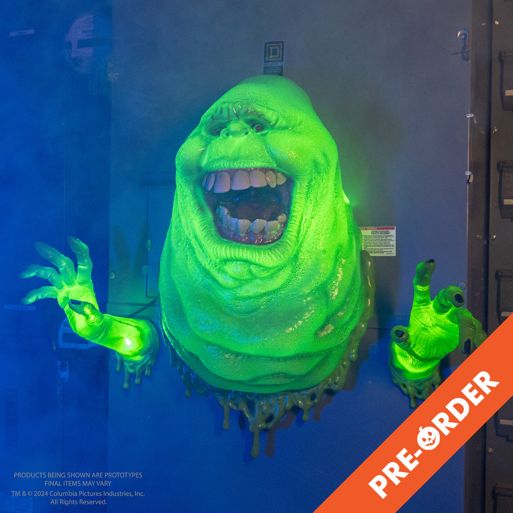 foggy background, orange diagonal banner bottom right, white text reads pre-order.  Wall mounted ghost. Bright green lighted ghost, lumpy blob with small eyes and nose, large open mouth showing large square teeth and tongue. hands separately mounted on wall lighted bright green with dark fingernails. slime dripping around edges at the wall.