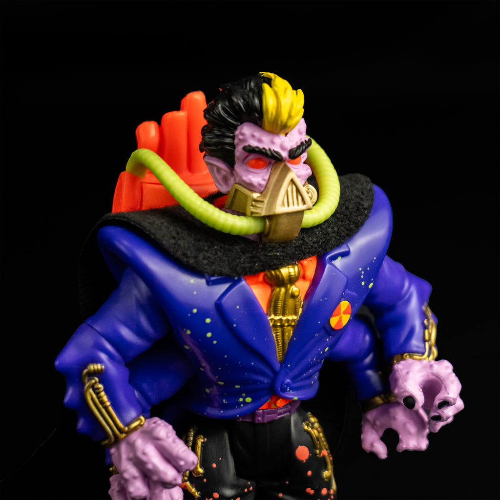 Black Background. Action figure, close-up slight right view. view. Short black hair, yellow stripe in the center front. Pale purple bumpy flesh. Black bushy eyebrows, red eyes. gold mask, triangular over nose and mouth, horizontal bands around lower jaw, yellow hoses on sides attached to orange backpack. Wearing orange shirt with a gold tie, blue jacket, four arms, black cape, black pants with orange splatter.