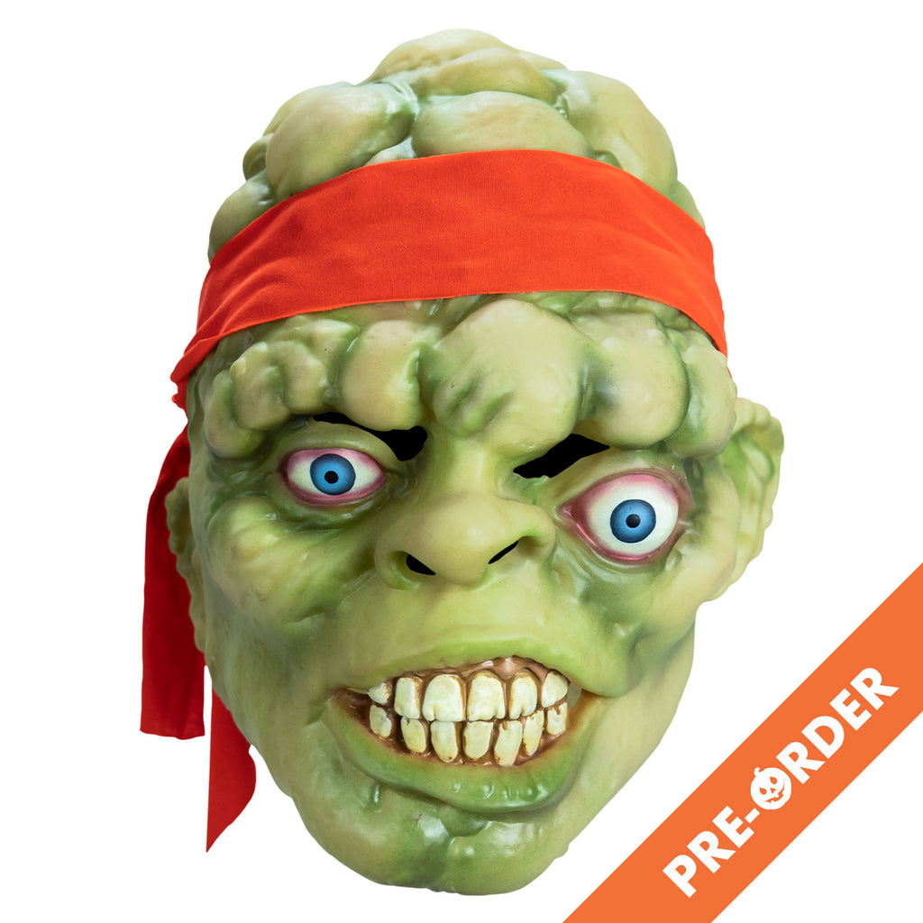 White background, orange diagonal banner at bottom right, white text reads pre-order. Mask, front view. Bald head, green lumpy flesh, with red-orange headband tied around forehead. Misaligned, red-rimmed blue eyes, crooked nose. Lips open showing large cracked teeth.