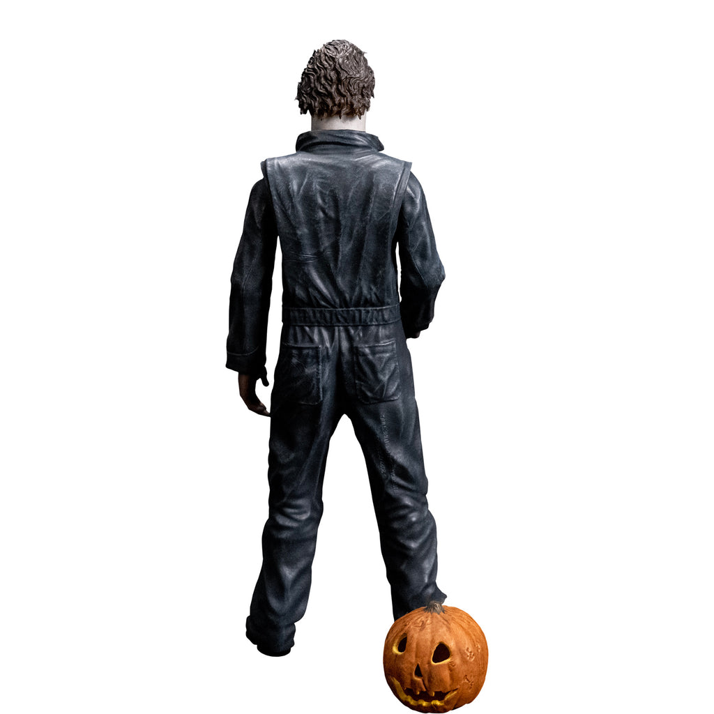 back view, Michael Myers 8 inch action figure. Wearing Halloween (1978) Michael Myers mask, dark coveralls, black boots. Orange jack o' lantern resting on ground.