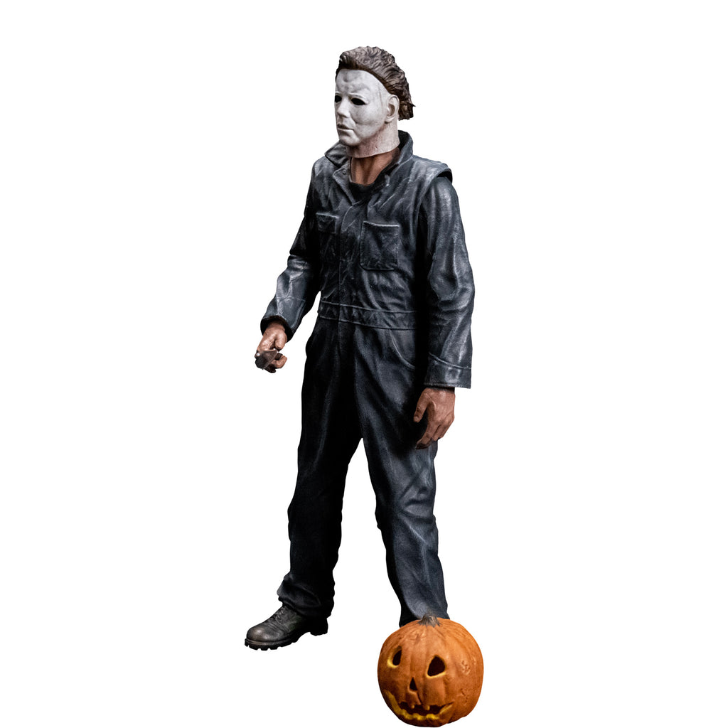 slight left view, Michael Myers 8 inch action figure. Wearing Halloween (1978) Michael Myers mask, dark coveralls, black boots. holding a kitchen knife in right hand. Orange jack o' lantern resting on ground in front of the figure