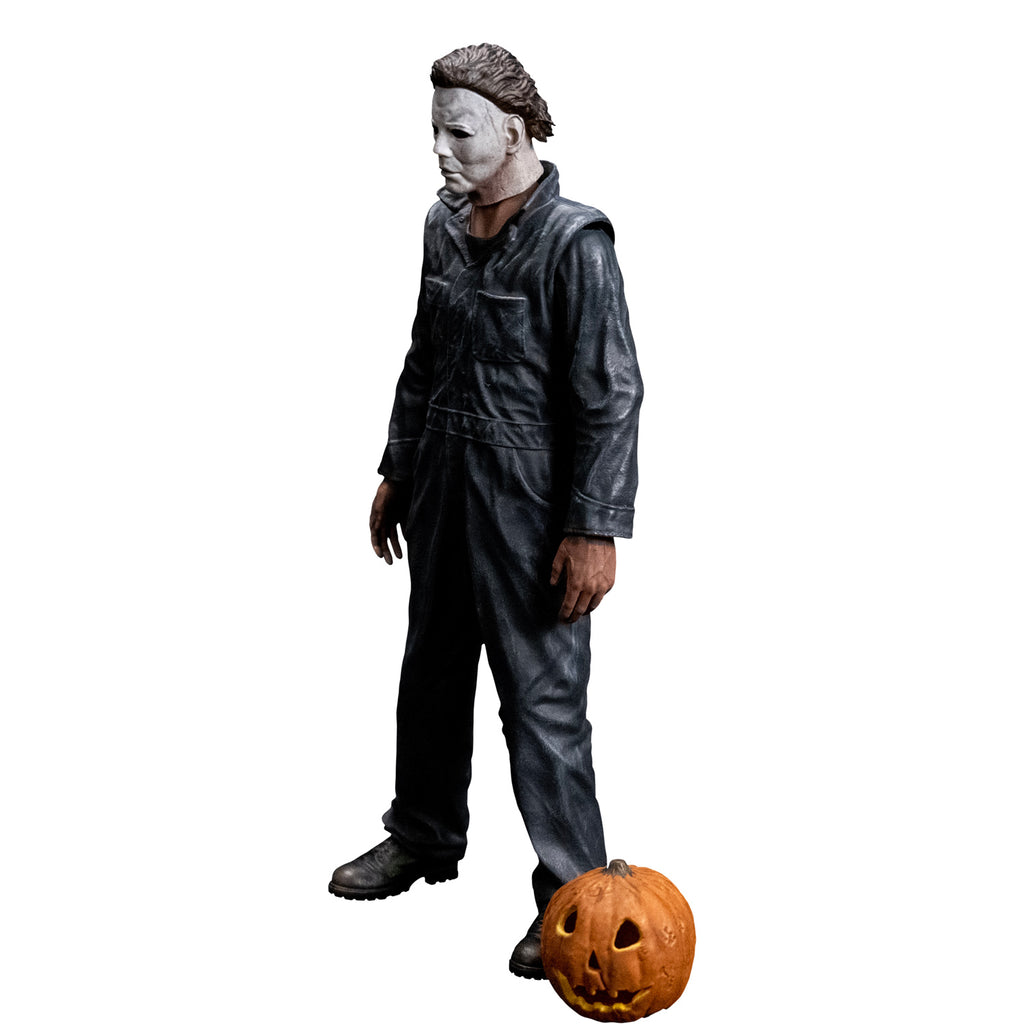 Slight left view, Michael Myers 8 inch action figure. Wearing Halloween (1978) Michael Myers mask, dark coveralls, black boots. arms at sides. Orange jack o' lantern resting on ground in front of the figure