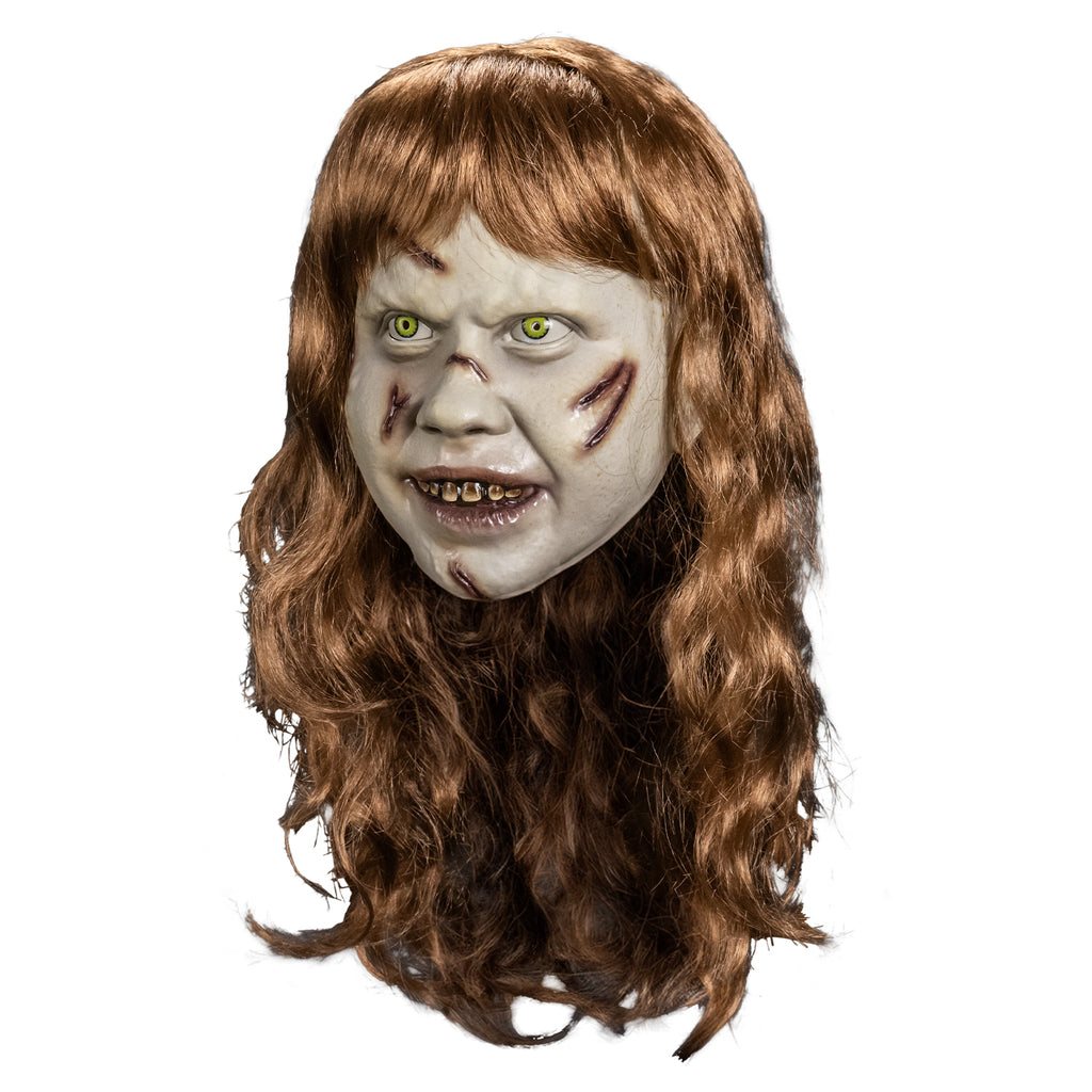 Plastic face mask left view. Girl's head, long, pale skin, light brown, wavy hair with bangs. Furrowed brow, no eyebrows, yelllow-green irises and small pupils in the eyes. red-brown wounds on right forehead, both cheeks, nose and chin. Mouth slightly open, showing dirty brown upper teeth, shiny wet looking lips.