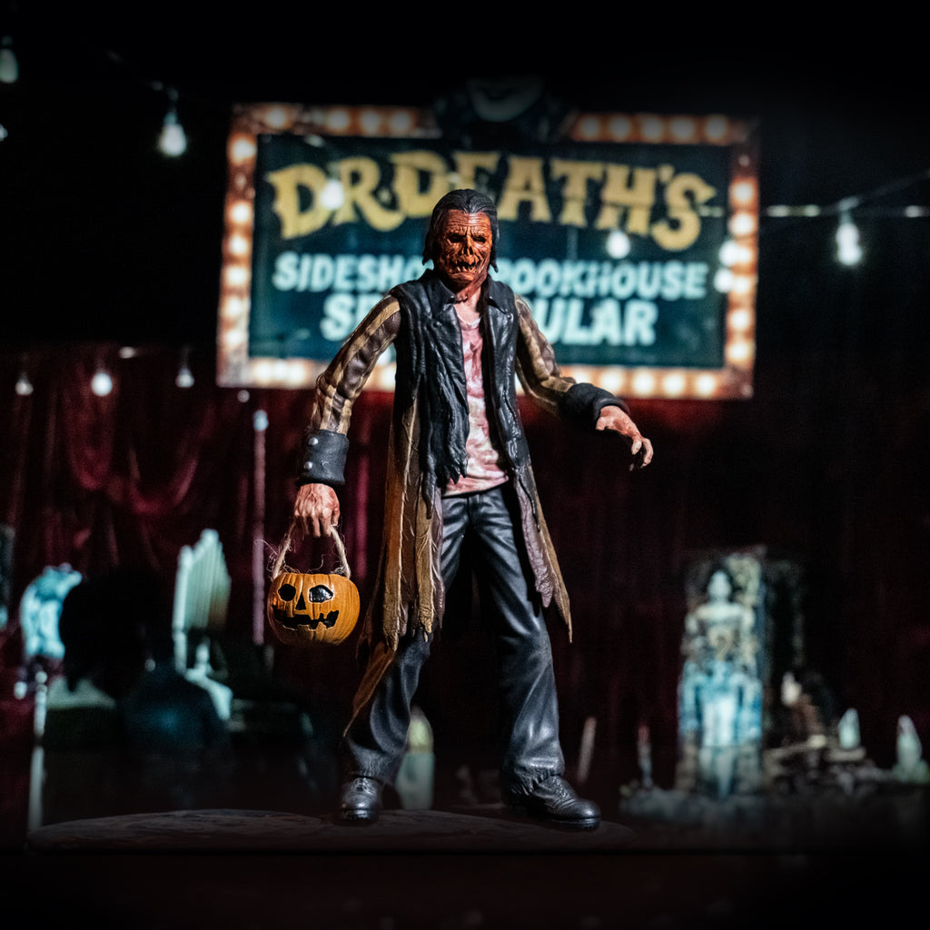 Glamour shot, blurry dark circus background.  Jacob Atkins figure in foreground, man with gory orange Jack O' Lantern-like face, dark slicked back hair. Wearing a bloodstained white shirt, brown and tan striped tattered coat with black cuffs and collar, black pants, black shoes. holding pumpkin candy pail in right hand.