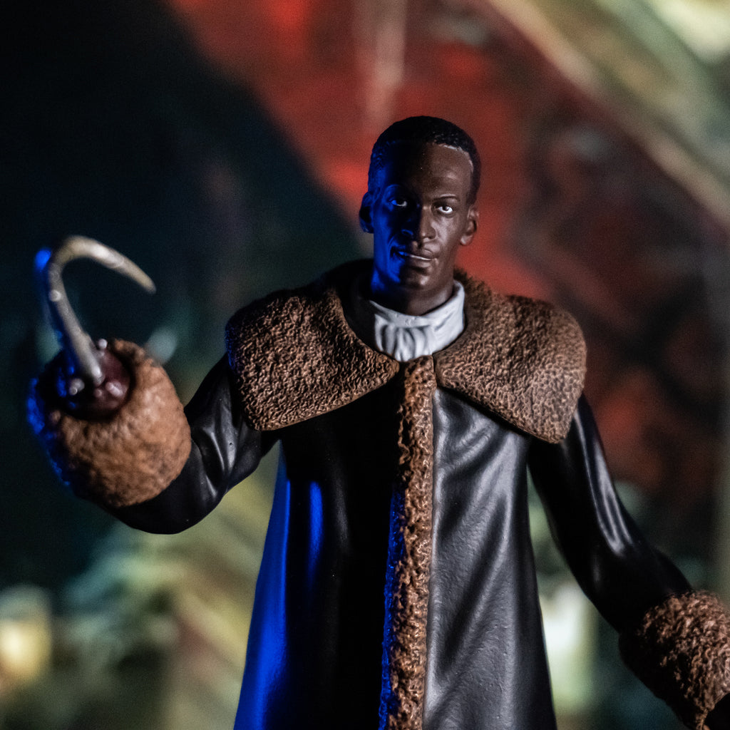 Glamour shot, blurry painted background. Candyman figure closeup front in the foreground. Man short brown hair, brown skin. wearing a white shirt under a full-length black leather coat with tan fur-trimmed large collar and cuffs. and a hook for his raised right hand.