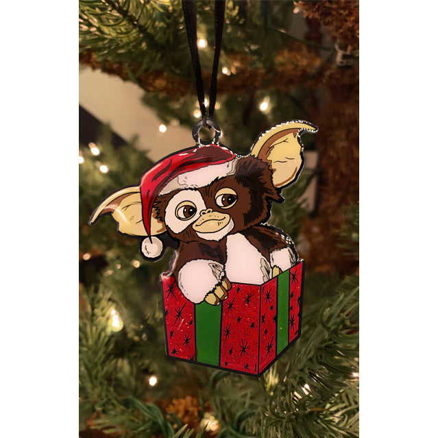 Gremlins Gizmo metal ornament hung on Christmas tree. Brown and White Gizmo, wearing Santa hat, sitting in red and green gift box,
