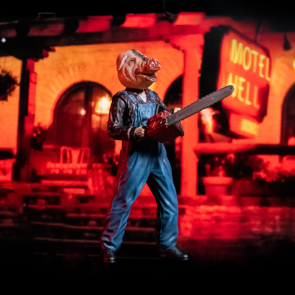 Orange Motel Hell glamour background. 8 inch figure slight right view. Person in foreground with bloodied pig head mask, mouth open. Wearing flannel print shirt, blue overalls, black boots. Holding red chainsaw with both hands.