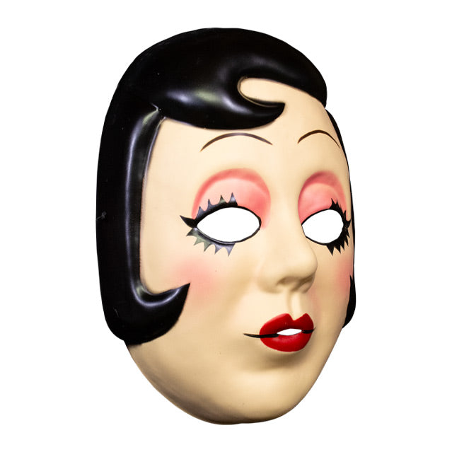Plastic face mask, right view. Woman's face, short black hair with curl on right side of forehead and at cheeks. Thin penciled eyebrows, empty eyeholes, spiky black eyelashes, pink eyeshadow. Small round red lips.