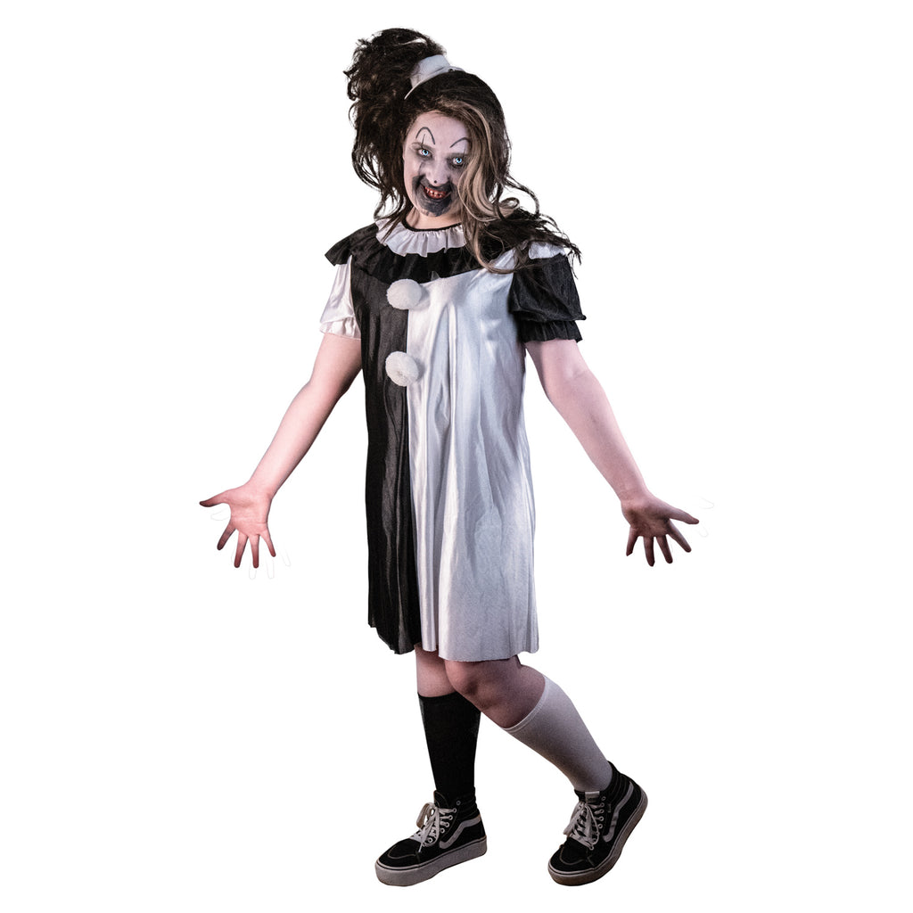 Pale girl costume. Evil grinning clown face with dark hair in messy, high, side ponytail held by white hat hairclip, black and shiny white, knee-length dress, ruffle at neck, white pompoms on chest. one black sock, one white sock.