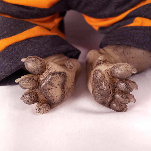 Close up view of paw like feet showing pads and claws.  Sparse black fur on legs.  Wearing gray and orange striped pajamas.