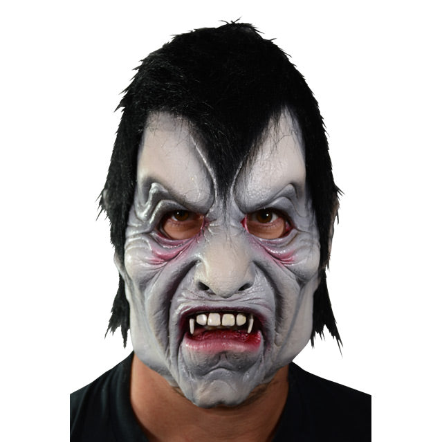 Front view. Man wearing vampire mask.  Pale gray skin, Black hair with deep widow's peak, creased skin around forehead, eyes and mouth.