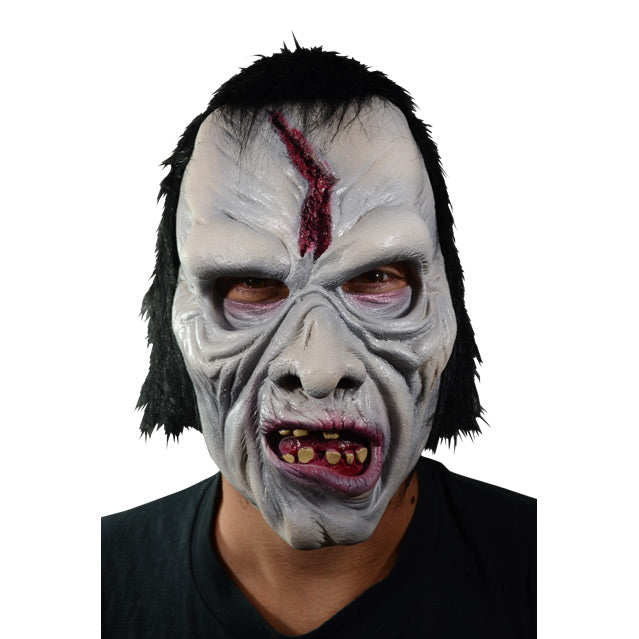 Front view. Man wearing mask.  Pale gray skin, wrinkled skin on forehead, cheeks and around mouth.  Gory gash in center of forehead.  gaping mouth with crooked dirty teeth, red gums, and tongue.