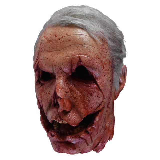 Head prop, left side view. Decapitated head, gray hair. mutilated face with cuts around eyes, nose and mouth to give the appearance of a jack o' lantern.