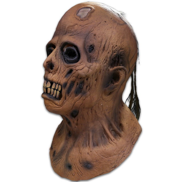 Mask left side view, head, neck and upper chest. Decaying zombie face, blackened spots on wrinkled skin, bald in front stringy sparse black hair in back, black-rimmed sunken eyes, ghastly mouth with large teeth.