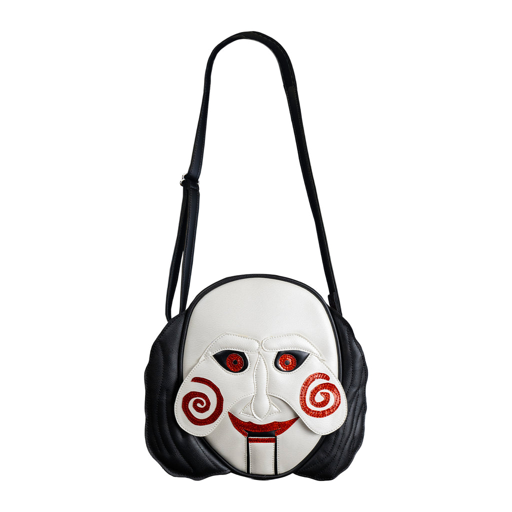 Bag, front view. Saw, Billy puppet face, black hair on sides, white face, black-rimmed red eyes, red spirals on cheeks, red lips on hinged ventriloquist dummy mouth.  Black adjustable strap.