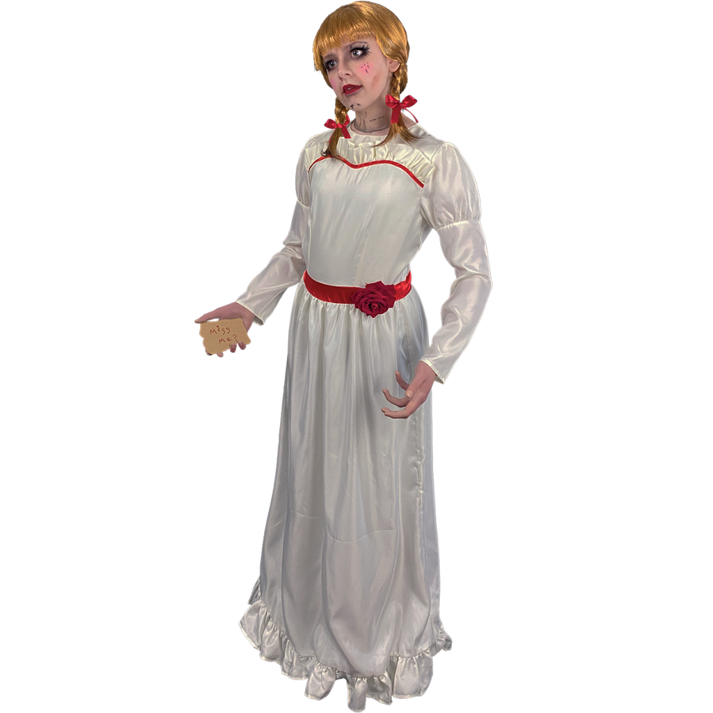 Person wearing Annabelle costume.  Blond wig with bangs, two braids tied with red ribbon.  White, floor-length dress with red trim at chest and red belt with rose. Holding card in hand, red handwritten text reads Miss me?