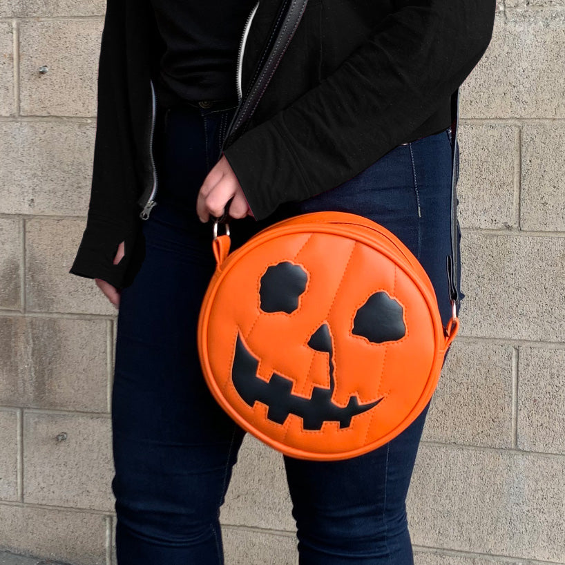 Body of person wearing Jack o' lantern purse. Front view. Orange and black with black strap.