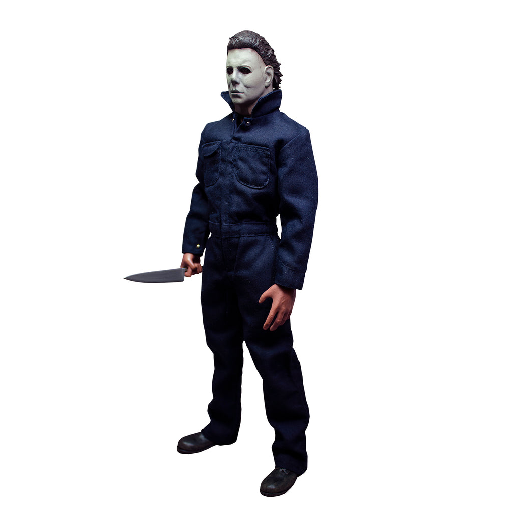 Michael Myers 12" figure. Left side view. White mask, brown hair, wearing blue coveralls, black boots, holding butcher knife in right hand.
