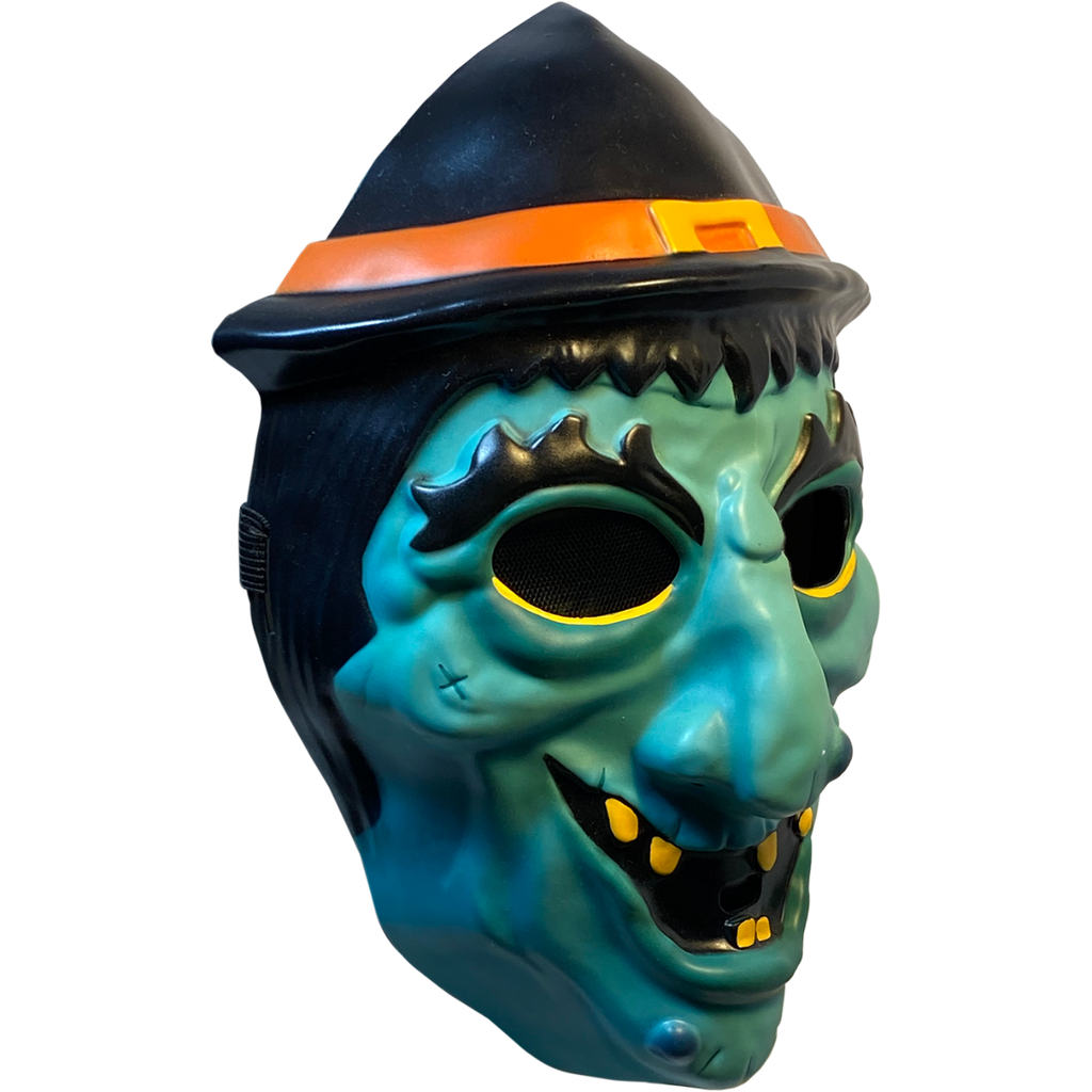 Plastic mask, right side view. Green witch face. Black hair, eyebrows and eyes. Black witch hat with orange band and yellow buckle. Yellow eyeliner under eyes. Grinning mouth with sparse yellow teeth.