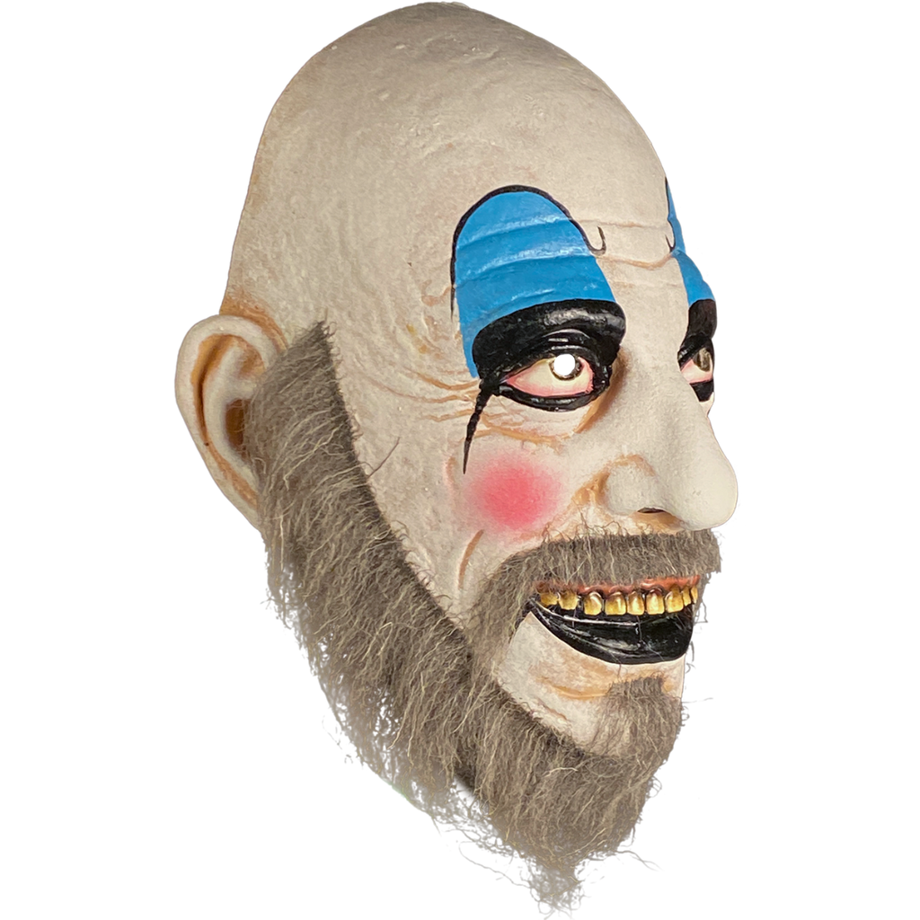 Mask, right side view. Bald man in white clown makeup, high black eyebrows, blue eyeshadow, black circles around eyes, pink spots on cheeks, large menacing grin, black bottom lip, full gray beard.