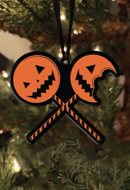 Metal ornament, hung on a Christmas tree.  Two lollipops crossed in an X.  Orange jack o' lantern faces with striped sticks, right lollipop has a bite taken out of it.