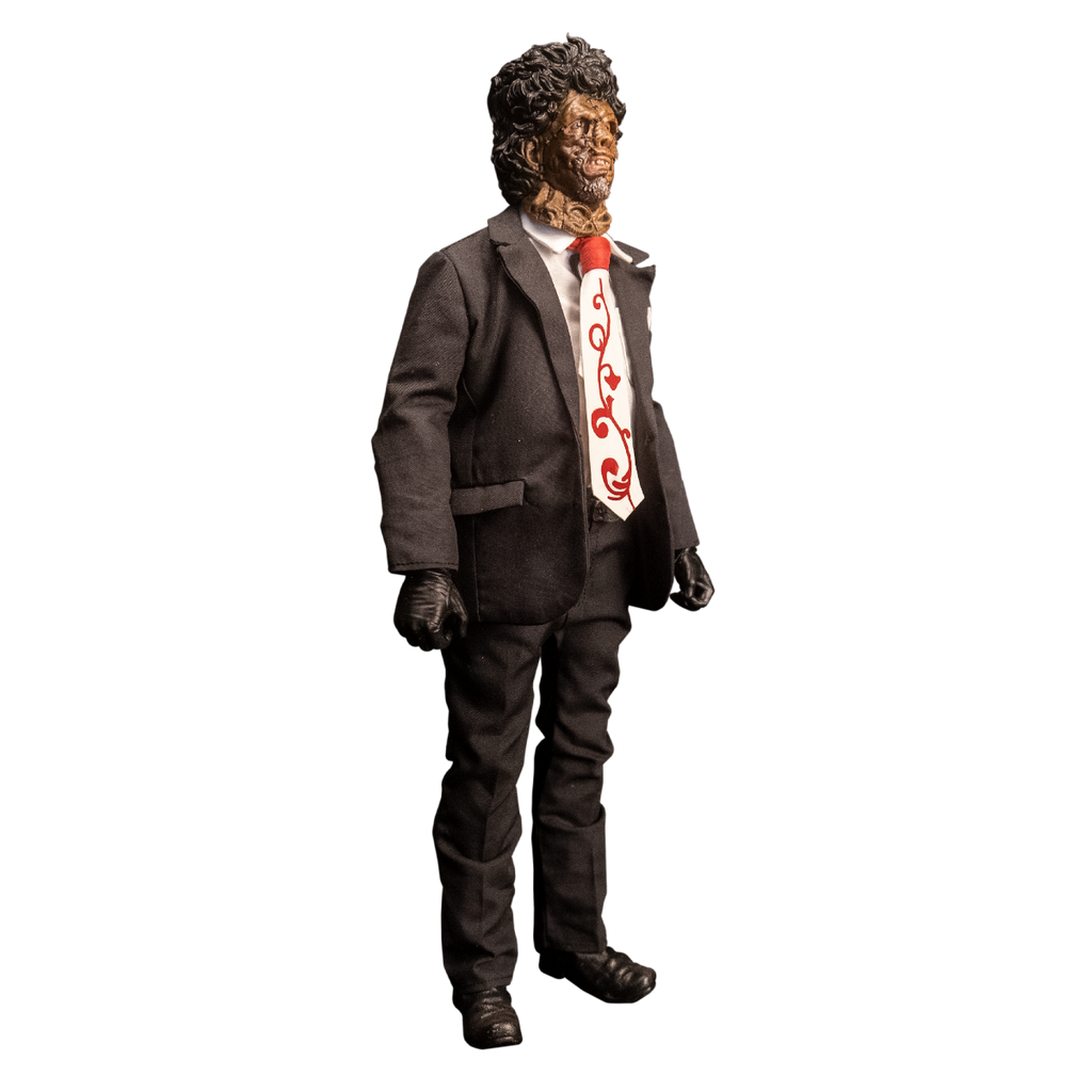 Action figure. Right view. Patchwork mask made of skin, brown hair. Wearing white collared shirt and orange and white necktie under dark suit coat, dark pants and belt. Black gloves and shoes.